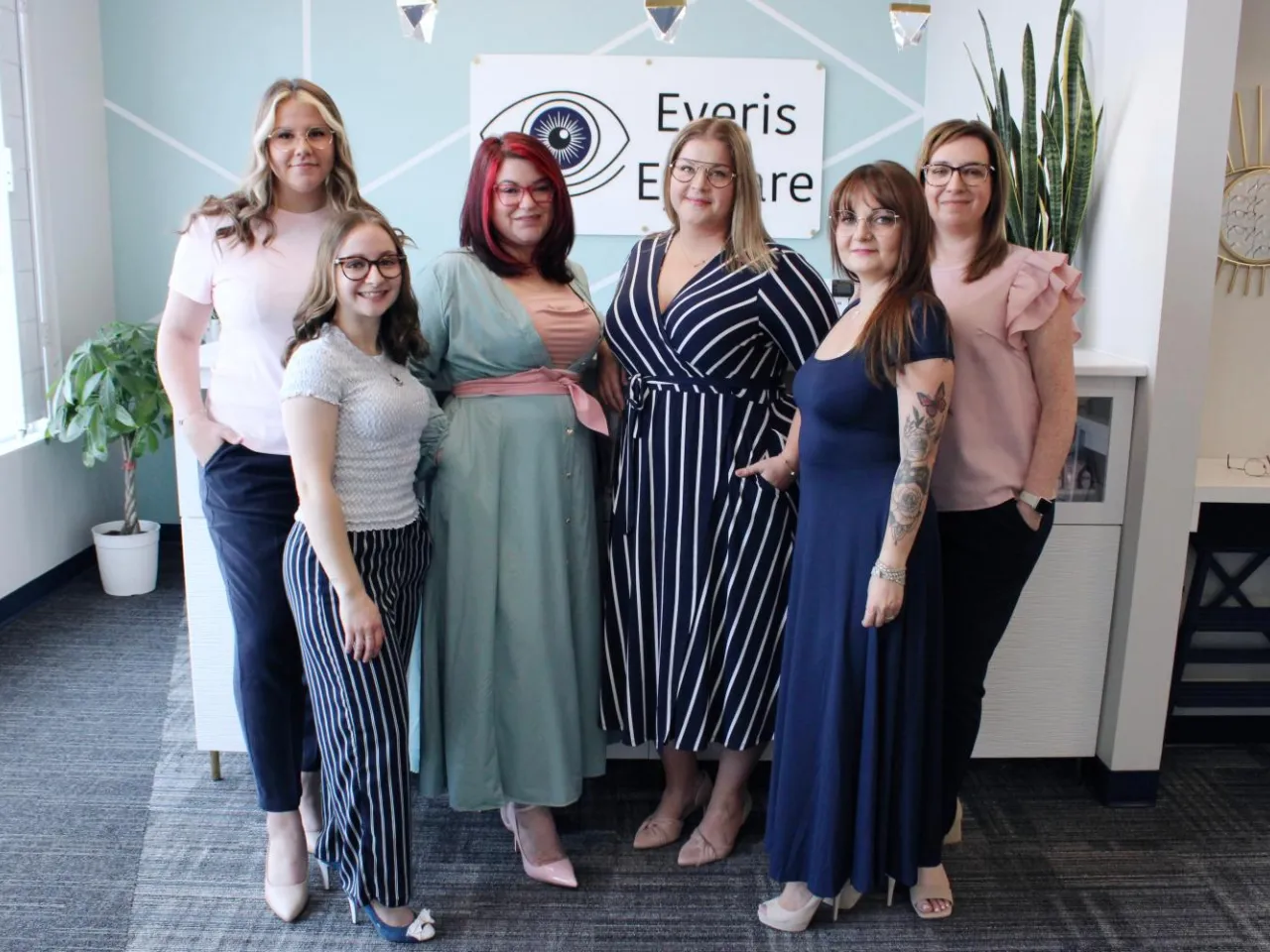 A professional group portrait of the Eyeris Eyecare team standing in front of their modern reception desk and clinic logo.